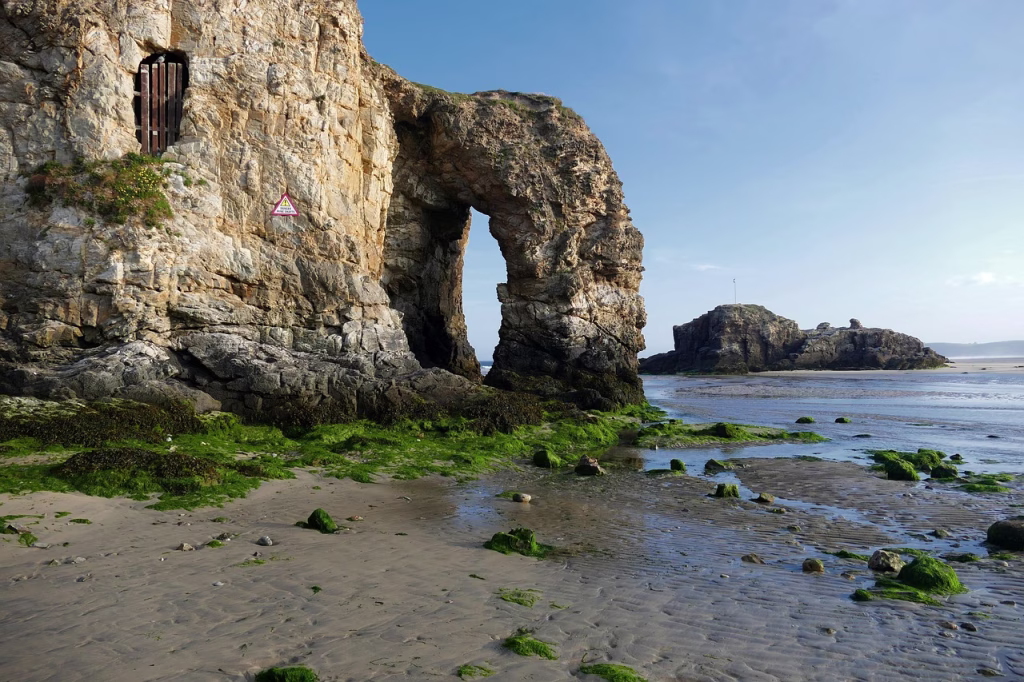 The natural rock arch at the promenade end of Perranporth beach, seen at low tide with seaweed-covered rocks and shallow pools